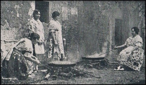 A very old caption of women dressed in the traditional Valencian customs cooking two Paellas